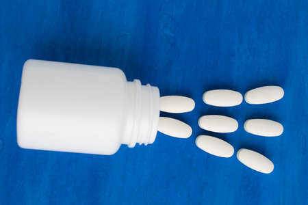 white pills spill out of a jar, on a blue backgroundの写真素材