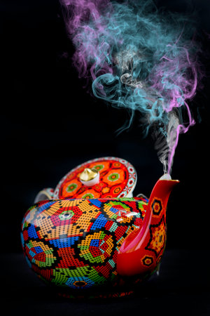 Colorful ceramic teapot on a black background with smoke.の写真素材