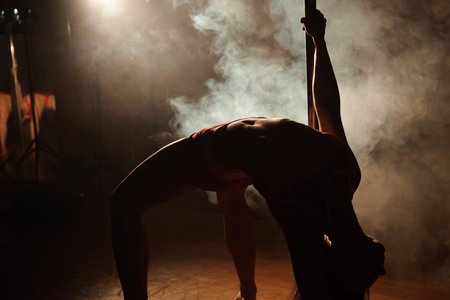 Young sexy woman exercise pole dance on a dark background