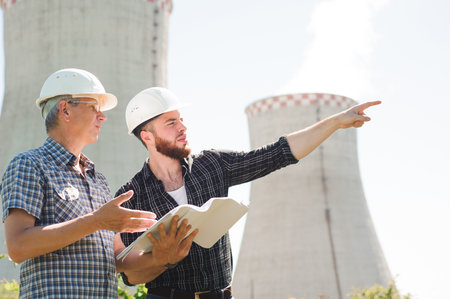 Male architects reviewing documents together at electric powerの写真素材