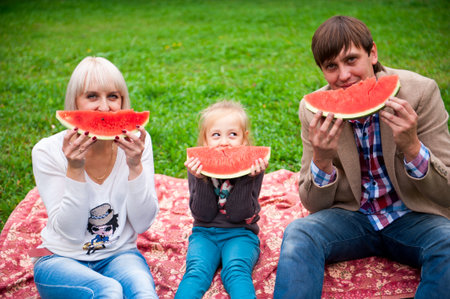 Family is eating a watermelon together in the park.の写真素材