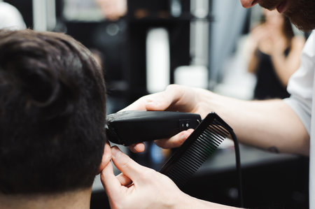 Master cuts hair and beard of men in the barbershop, hairdresser makes hairstyle for a young man.の写真素材