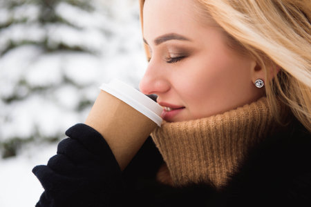 Portrait of european style fashionable woman drinking coffee in the winter park.の写真素材
