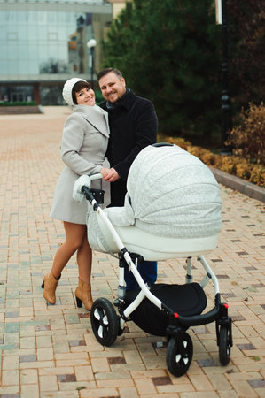 Family walk in the autumn park with a pram. Mom, dad and baby outdoors