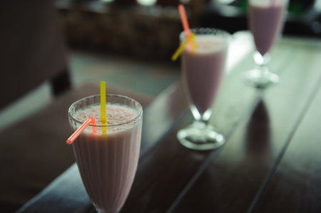 Three jars of pink berry milkshakes with straws on old wooden table.の写真素材