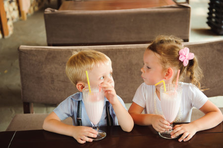 Little boy and girl drinking milkshakes in a cafe outdoors.の写真素材