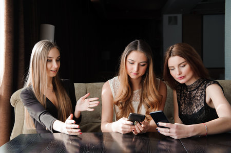 always connected, internet addiction, young girls in cafe looking at their smartphones, social network concept.の写真素材