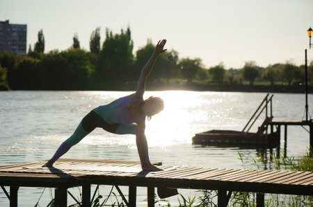 Young woman doing yoga in morning park near lake.の写真素材