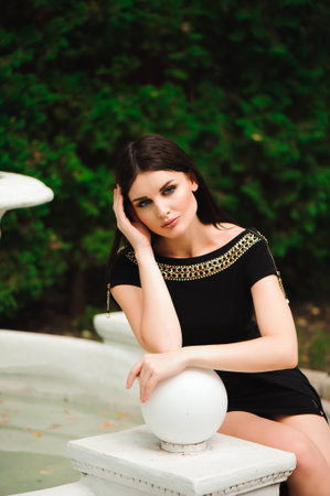 Young beautiful stylish girl walking and posing in short black dress in city near fountains. Outdoor summer portrait of young classy woman.の写真素材