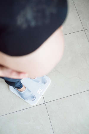 Pregnant woman standing on a scales at home.