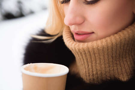 Portrait of european style fashionable woman drinking coffee in winter park.