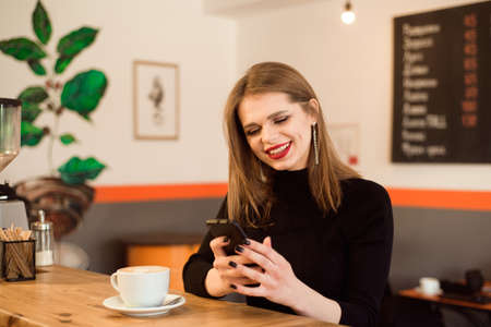 happy Caucasian female watching her photo on cell telephone while relaxing in cafe.の写真素材
