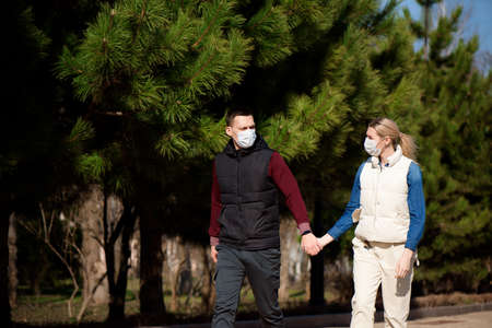 Young European man and woman in protective disposable medical mask walking outdoors