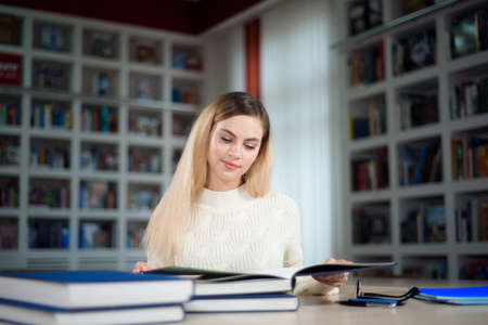 Portrait of clever student with open book reading it in college library.