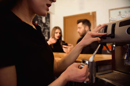 Professional female barista holding metal jug warming milk using the coffee machine.の写真素材