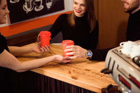 Close up hands taking cup of hot coffee from barista in confectionary shop.