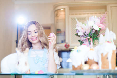 Easter holidays. A young woman in a blue apron decorates eggs and prepares gifts for Easter.