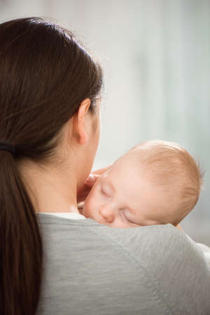 Young mother holding her newborn child. Mom nursing baby. Woman and new born boy relax in a white...
