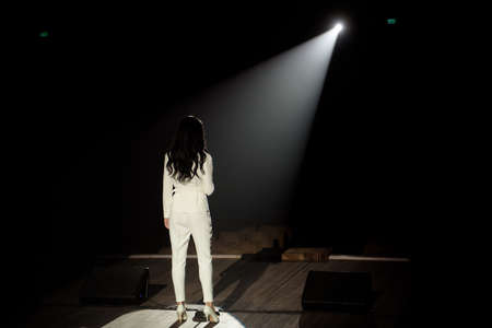 Back view of a singer with microphone singing a song on stage in white lights.の写真素材
