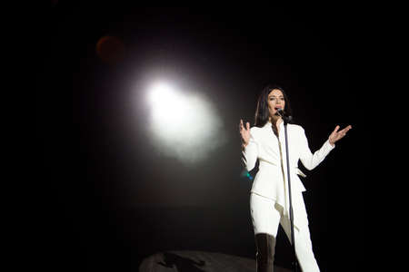Singer woman on stage with black background in a beam of white light.