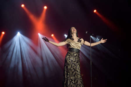 Singer in a dress on stage in the rays of bright light with smoke.