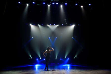 Silhouette of singer standing on stage at microphone in night club.の写真素材