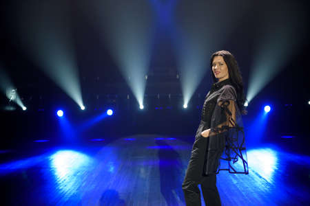 Beauty woman artist on the stage. Dark background, smoke, blue spotlights.