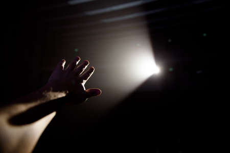 Mans hand in a ray of light on a black background.の写真素材