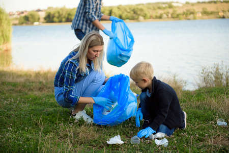 volunteering, charity, people and ecology concept, volunteers using garbage bag while collecting litterの写真素材