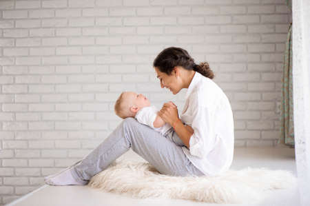 Mom and baby boy in diaper playing in sunny bedroom. Family haviの写真素材
