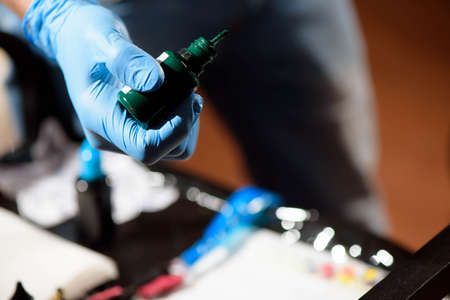 Tattoo artist at work. Close up. Man creating picture on hand with it in salonの写真素材