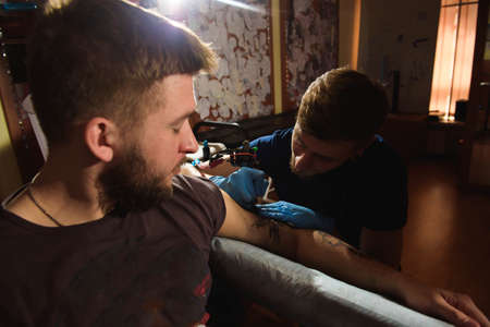 Professional tattoo artist makes a tattoo on a mans hand.の写真素材
