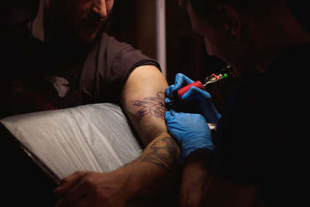 Tattoo artist makes a tattoo on a mans hand. Man creating picture on hand with it in salonの写真素材