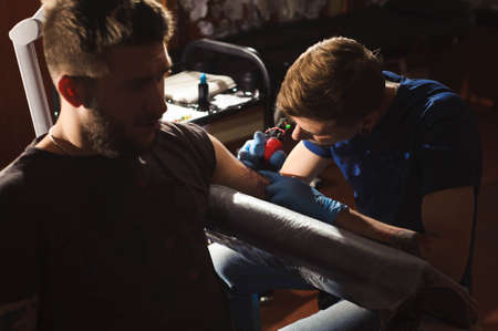 Tattooist makes a tattoo. Man creating picture on hand with it in salonの写真素材