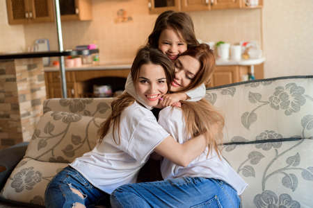 Two sisters and little daughter smiling and hugging at home interior background.の写真素材