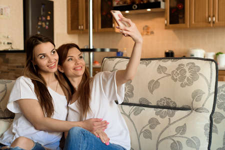 Close up portrait of two excited girlfriends with mobile phones, laughing. Happy joyful female friends resting at home, enjoying talks, having fun.の写真素材