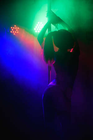 Beautiful slim girl with pylon. Female pole dancer woman dancing on a pole on a black background.の写真素材