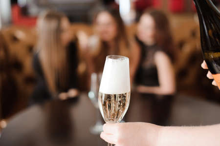 Man fills glasses of champagne for three beautiful young women in restaurantの写真素材