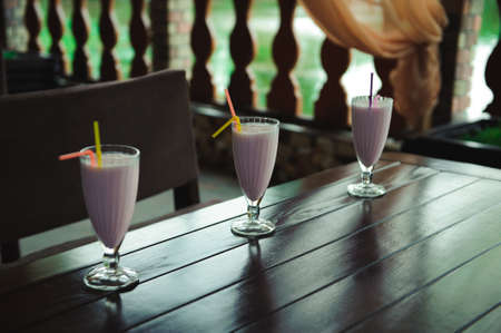 Three jars of pink berry milkshakes with straws on old wooden table.の写真素材