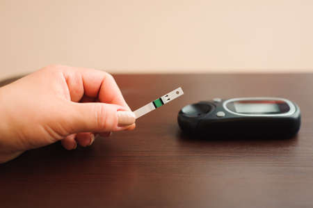 Diabetic patient doing glucose level blood test using ultra mini glucometer and small drop of blood from finger and test strips.の写真素材