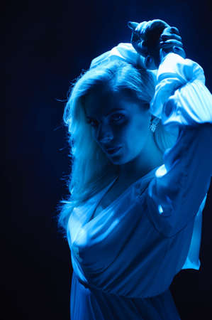 Beautiful moman in flying white dress in the light of blue light. Flowing fabric. Light white cloth flying in the wind.の写真素材