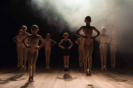 Happy children doing ballet jump on a dark lighted scene.