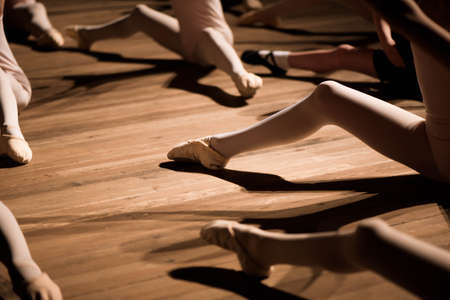 Pretty young girl and boy sitting on stage having stretching and training for ballet dancesの写真素材