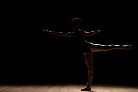 Cute little ballerina in dark ballet costume dancing on the stage. Kid in dance class. Child girl is studying ballet.の写真素材