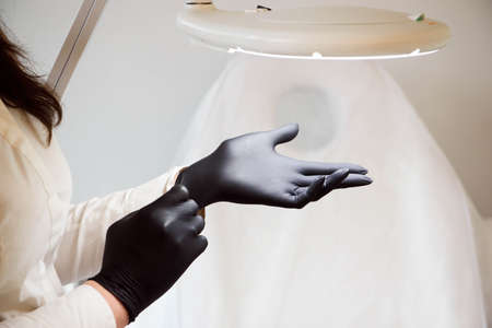 Doctor beautician wears sterile black gloves prepares to receive clients.