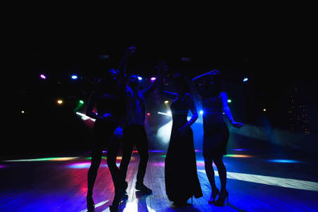 Silhouettes of dancing people in club in front of bright stage lights - disco concept.の写真素材