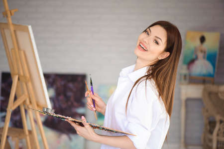 Young female artist painting picture in studio.