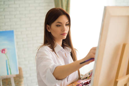 Cute girl artist paints on canvas painting on the easel. Model in the studio.の写真素材