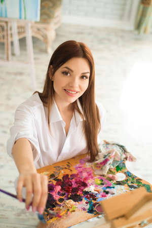 Cute girl artist paints on canvas painting on the easel. Model in the studio.の写真素材