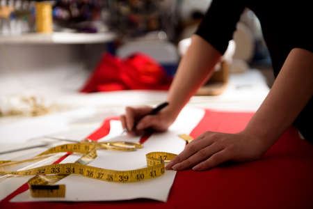 Young dressmaker woman sews clothes on sewing machine.